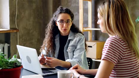 Junge-Unternehmer-spricht-beim-Sitzen-am-Schreibtisch-zusammen-mit-ihrem-Partner-im-modernen-Büro.-Frauen-planen-neues-Projekt.-Erfolgreiche-Zusammenarbeit-Konzept.