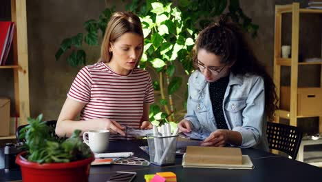 Jóvenes-diseñadores-creativos-son-mirar-fotos-con-atención-y-discutir-mientras-sentados-juntos-en-la-mesa.-Bandeja-de-tiro-de-la-oficina-de-estilo-moderno-loft.