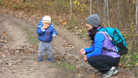 A-mother-feeds-her-little-child-in-autumn-forest-on-the-trail.