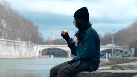 einsame-junge-Obdachlose-isst-einen-Apfel,-den-Fluss-zu-betrachten