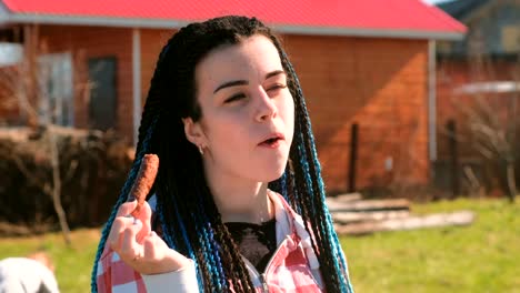 Woman-eating-meat-sausage-in-the-backyard-in-the-spring-on-a-Sunny-day.-Her-son-plays-around.