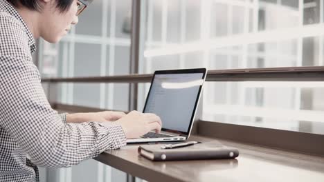 Young-Asian-business-man-using-laptop-computer-in-working-space-with-smartphone-and-notebook-on-wooden-desk.-Male-hand-typing-on-laptop-keyboard.-Freelance-lifestyle-in-digital-age-concept.