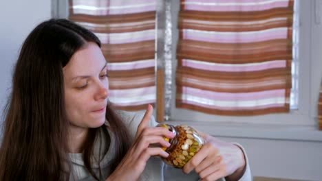 Woman-eating-honey-from-a-jar-of-nuts-in-honey-with-finger.