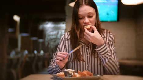 Junge-schöne-Frau-Brünette-schmiert-Pastete-auf-ein-Stück-Brot-im-Café-mit-Messer.-Und-sie-isst-Sandwich.