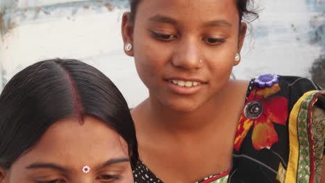 Extreme-close-tilt-down-to-two-beautiful-women-in-traditional-Indian-clothes-on-a-mobile-phone-sharing-a-photo-video-with-each-other-at-the-comfortable-of-their-home-face-portrait-cute-hands-closeup