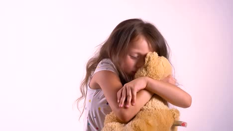 Little-cute-girl-hugging-her-plush-teddy-bear-and-standing-isolated-on-pink-studio-background