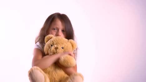 Little-cute-girl-hugging-her-plush-teddy-bear,-kid-embracing-toy,-standing-isolated-on-bright-pink-studio-background