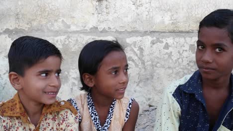 Three-Indian-kids-sitting-and-talking-to-each-other-and-then-looking-towards-the-camera