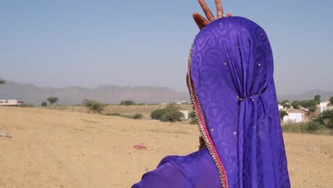 Nomadische-Frau-tanzt-auf-einer-Sanddüne-in-Rajasthan-mit-Kamelen-im-Hintergrund