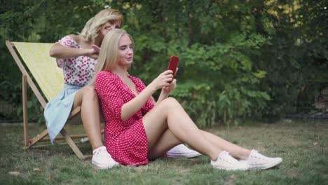 two-friends-have-a-good-time-in-the-park,-they-use-a-smartphone