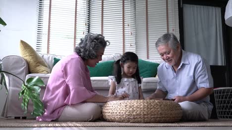 Couple-senior-and-kids-girl-playing-puzzle-games-together-in-living-room-at-home.-Concept-of-caucasian-family,-education,-growing-learn-and-development-of-age.-4k-resolution.