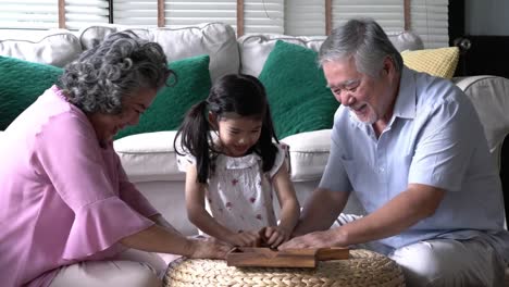 Couple-senior-and-kids-girl-playing-puzzle-games-together-in-living-room-at-home.-Concept-of-caucasian-family,-education,-growing-learn-and-development-of-age.-4k-resolution.