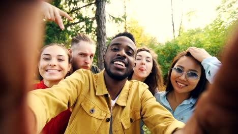 Point-of-view-shot-of-friends-taking-selfie-in-park-looking-at-camera,-making-funny-faces-and-laughing-having-fun.-Modern-technology,-friendship-and-nature-concept.