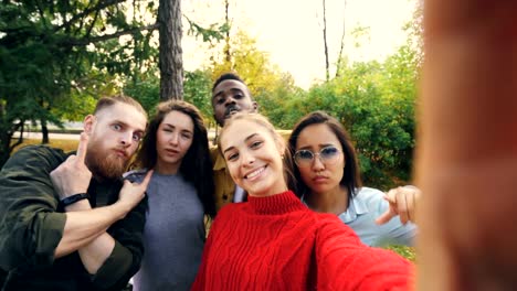 Sicht-der-jungen-Frau-Haltevorrichtung-mit-Kamera-und-Selfie-mit-multi-ethnischen-Freundesgruppe-im-Park-im-Herbst-gedreht.-Konzept,-Fotografie-und-Menschen.