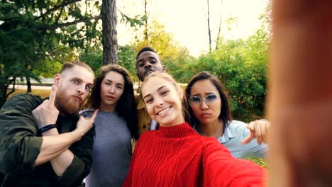 Point-of-view-shot-of-young-woman-holding-device-with-camera-and-taking-selfie-with-friends-multi-ethnic-group-in-park-in-autumn.-Photography-and-people-concept.