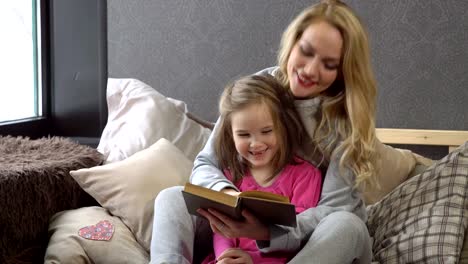 Mother-and-daughter-sitting-on-the-bed-in-an-embrace-and-reading-a-book.