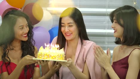 Young-woman-birthday-girl-is-making-wish,-blowing-candle-on-cake-and-clapping-hands-while-her-friends-are-congratulating-her-at-the-party.--Slow-Motion