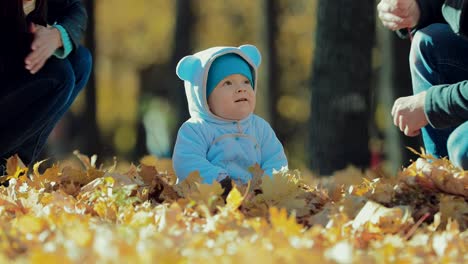 Small-child-sits-in-the-autumn-leaves.-Dad-gives-sniffing-autumn-leaf-to-his-son