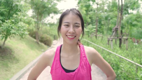 Mujer-saludable-hermosa-joven-asiática-corredor-sintiendo-feliz-sonriendo-y-mirando-a-la-cámara-después-de-correr-en-la-calle-en-parque-urbano-de-la-ciudad.-Ajuste-del-estilo-de-vida-y-ejercen-de-las-mujeres-activas-en-el-concepto-de-Parque-de-la-ciudad