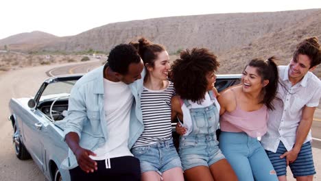 Friends-on-a-road-trip-take-a-roadside-break-sitting-on-car