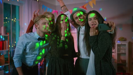 Glückliche-Gruppe-von-jungen-Leuten-unter-kollektiven-Selfie-auf-wilde-Hausparty.-Neon-Licht,-Disco-Kugel-und-lustige-Kostüme.