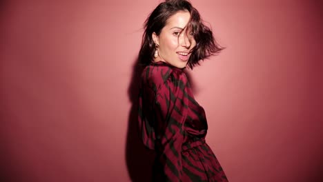 Brunette-happy-woman-dance-with-balloons-and-confetti-in-pink-background-wear-red-dress