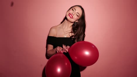 Brunette-happy-woman-dance-with-balloons-and-confetti-in-pink-background-wear-red-dress