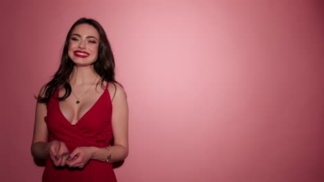 Brünette-Frau-glücklich-geben-Luft-Kuss-mit-Konfetti-in-rosa-Hintergrund-tragen-rote-Kleid