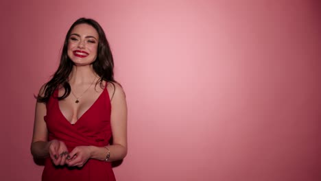 Brunette-happy-woman-give-air-kiss-with-confetti-in-pink-background-wear-red-dress