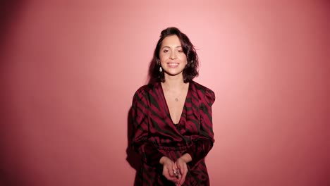 Brunette-happy-woman-throw-up-and-laugh-to-camera-with-confetti-in-pink-background-wear-red-dress