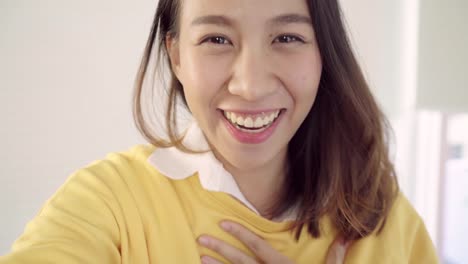 Asian-blogger-woman-using-smartphone-recording-vlog-video-in-living-room-at-home,female-enjoy-funny-moment-while-lying-on-the-sofa-when-relax-at-home.-Lifestyle-blogger-making-video-at-home.