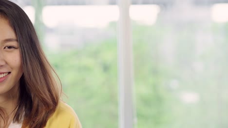 Teenager-Asian-woman-feeling-happy-smiling-and-looking-to-camera-while-relax-in-her-living-room-at-home.-Beautiful-Asian-young-female-using-relax-time-at-home-concept.