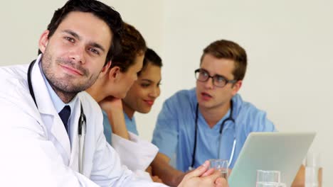 Doctor-smiling-at-camera-while-colleagues-are-talking