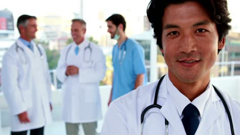 Doctor-smiling-at-camera-with-team-behind-him