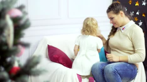 Madre-joven-feliz-jugando-con-su-bebé-dulce-en-un-decorado-cerca-del-árbol-de-Navidad