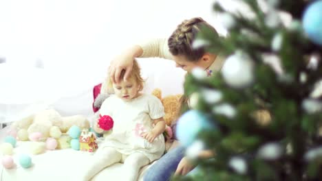 Madre-joven-feliz-jugando-con-su-bebé-dulce-en-un-decorado-cerca-del-árbol-de-Navidad