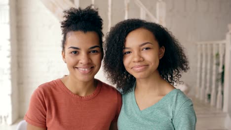 Closeup-portrait-of-two-beautiful-african-american-girls-laughing-and-looking-into-camera.-Women-show-emotions-from-serios-face-to-laugh-at-home