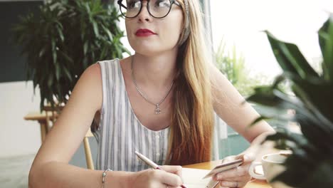 Young-pretty-woman-writing-information-from-card-to-notebook-.-Female-writing-in-cafe.