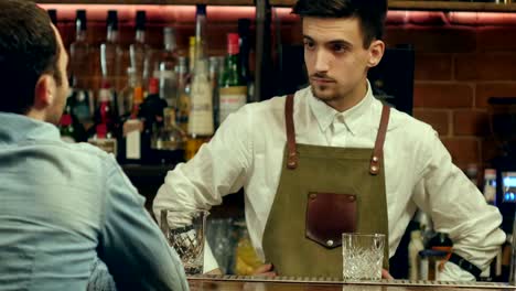 Young-bartender-talking-and-smiling-to-a-male-visitor