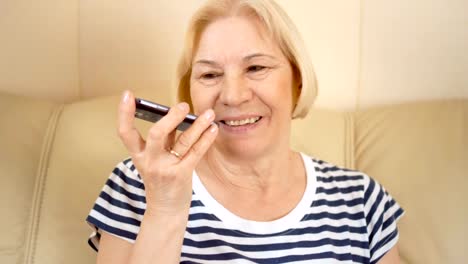 Fröhliche-gut-aussehende-senior-Frau-sitzt-auf-dem-Sofa-zu-Hause.-Sprechen-auf-ihrem-smartphone