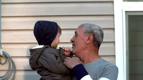 Grandfather-and-grandson-talking,-smiling,-having-fun,-looking-to-camera-outdoor.-Old-man-holding-on-hand-little-boy.-4K