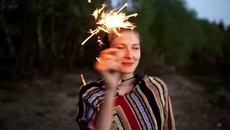 Portrait-of-young-smiling-woman-with-sparkler-celebrating-at-beach-party