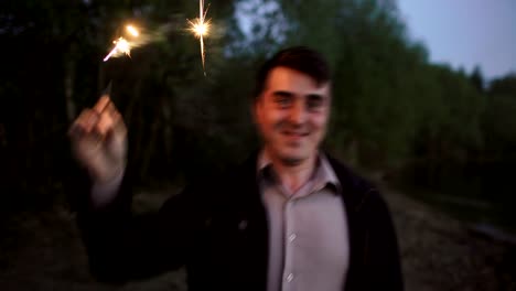 Portrait-of-young-smiling-man-with-sparkler-celebrating-at-beach-party