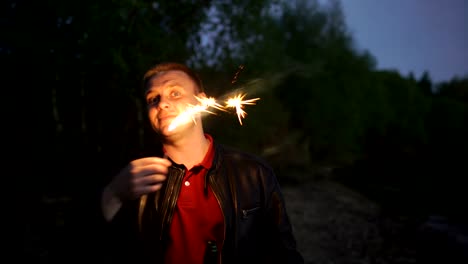 Portrait-of-young-smiling-man-with-sparkler-celebrating-at-beach-party