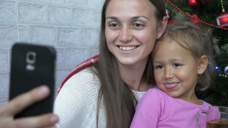 Feliz-madre-e-hija-plaing-el-mono-y-selfie-junto-al-árbol-de-Navidad