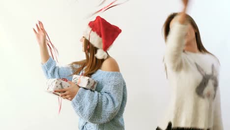 Two-girlfriends-waving-a-red-ribbons-and-dances-with-gifts-at-white-background