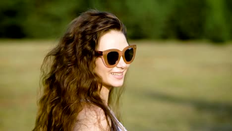 Mujer-joven-con-gafas-de-sol-y-posando-felizmente-en-naturaleza-mirando-lejos-de-luz-del-sol