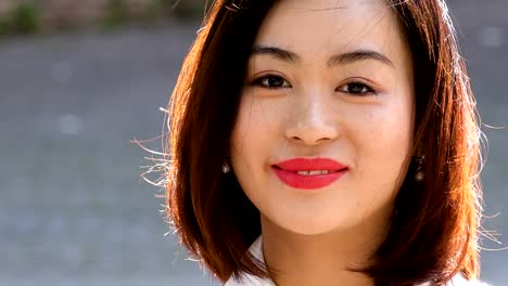 Beautiful-young-Asian-woman-turns-her-head-and-smiles-at-the-camera,close-up