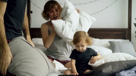 Familia-feliz-con-la-hija-Linda-jugando-y-lucha-almohadas-en-la-cama-en-casa