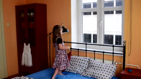 Cute-little-girl-dances-and-jumps-on-a-bed.-Small-girl-wears-flowered-dress.-Childhood-concept